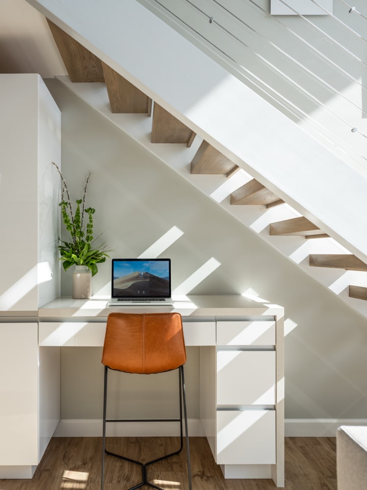 A desk with an open laptop below a staircase.