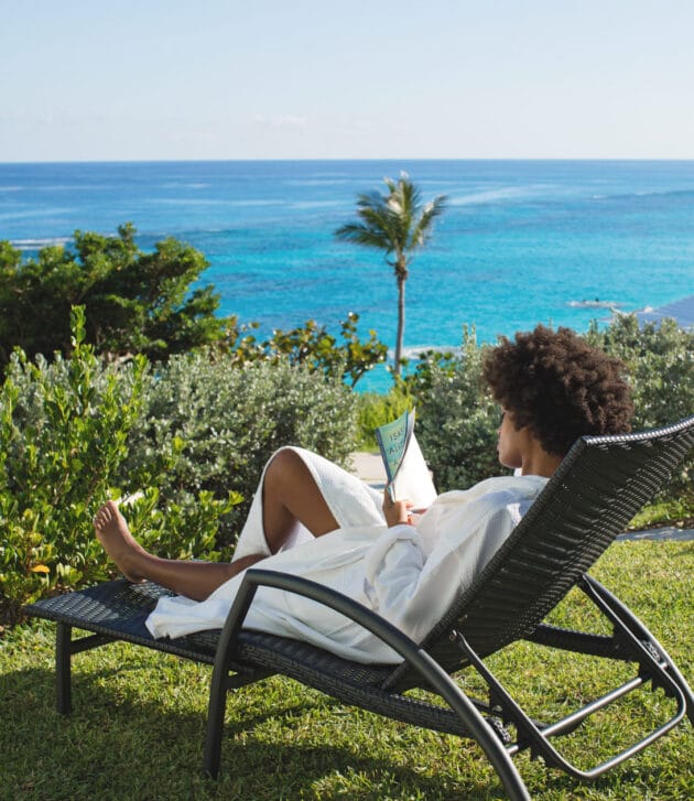 A woman relaxing in a lawn chair overlooking the ocean.