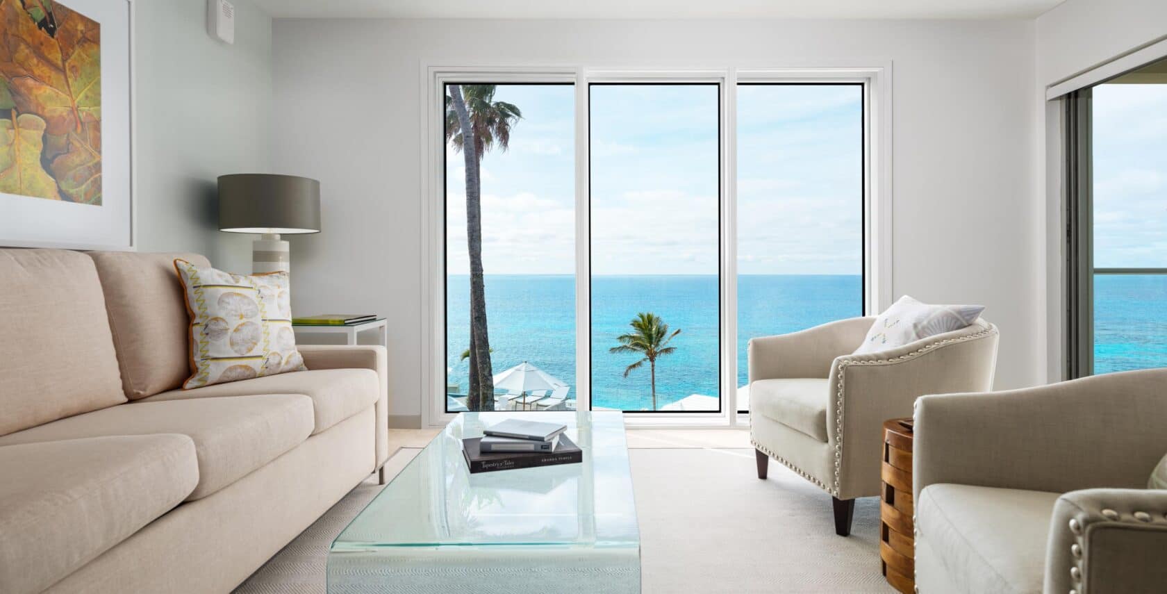 A living area with couches, a glass coffee table, and glass doors with an ocean view.