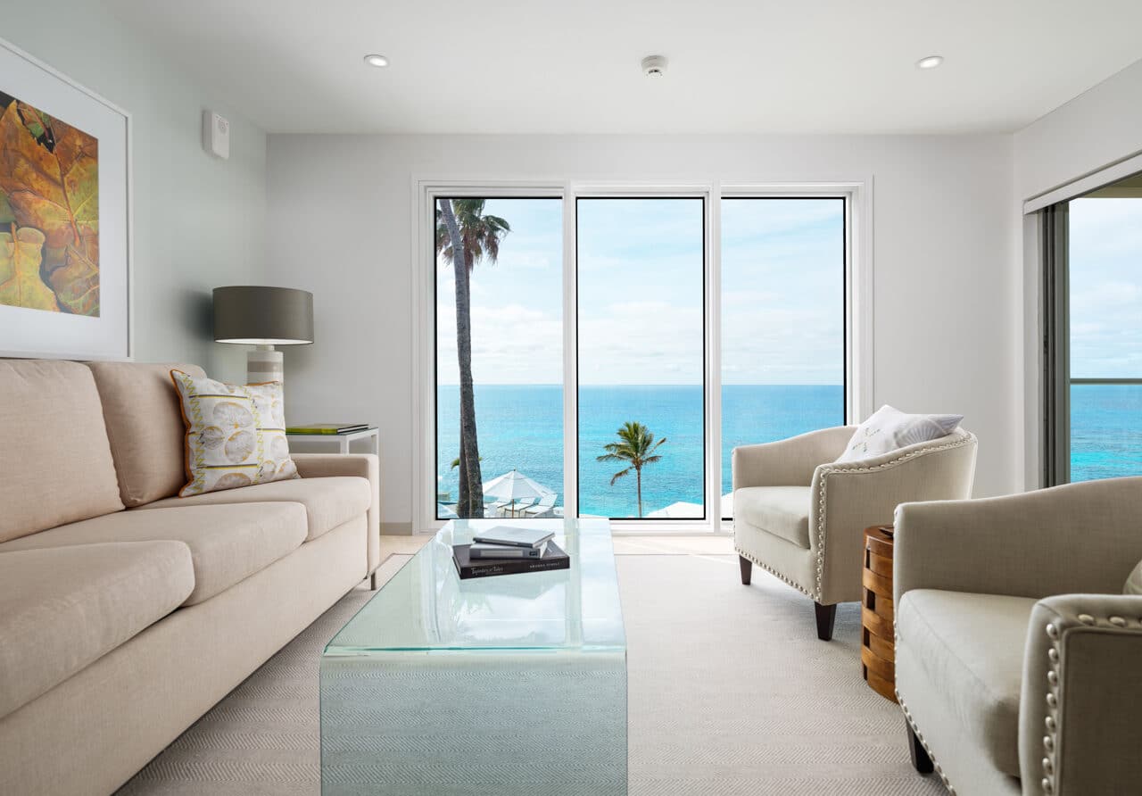 A living area with couches, a glass coffee table, and glass doors with an ocean view.