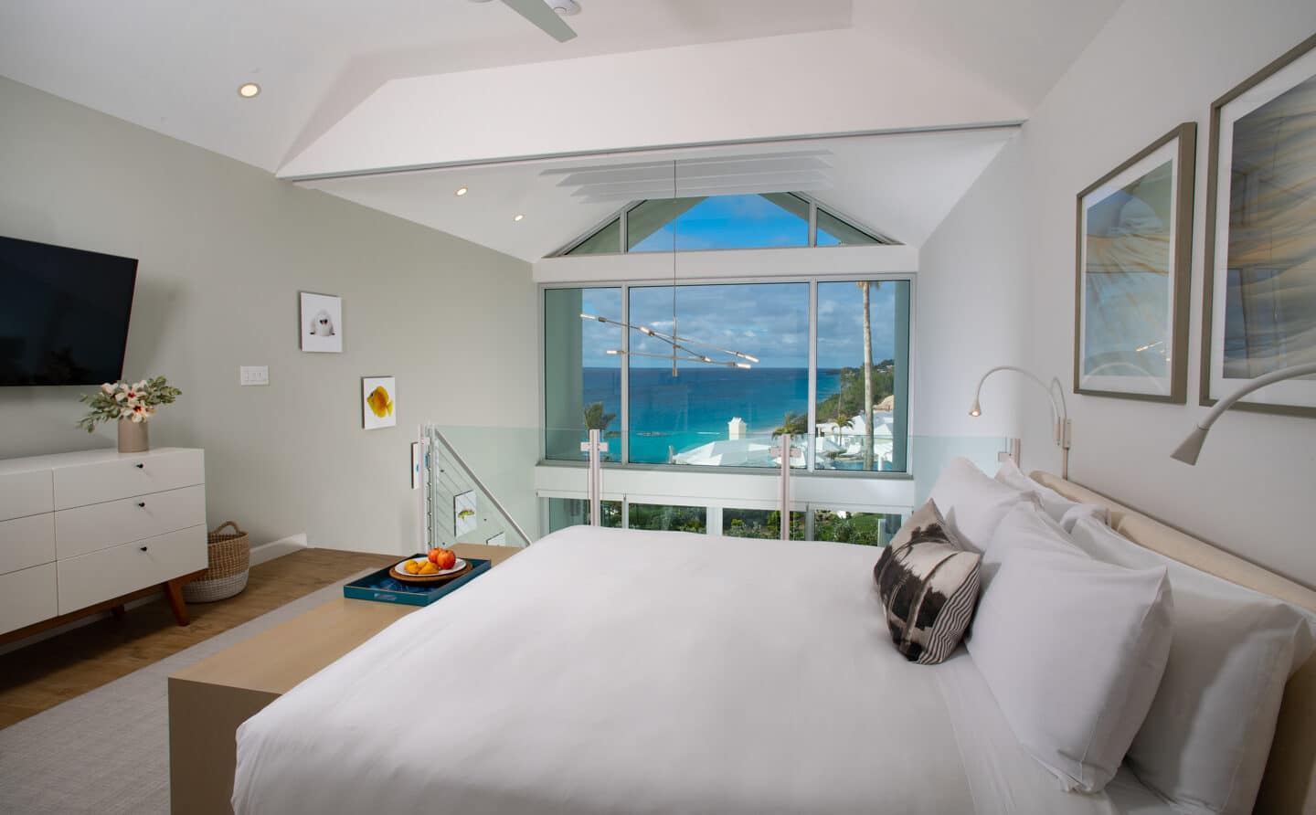 A loft bedroom with a TV and a large window with an ocean view.