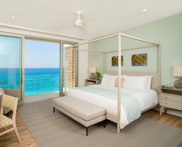 A bedroom with a canopy bed and large glass sliding doors displaying an ocean view.