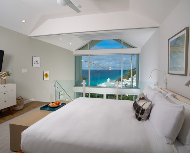 A loft bedroom with a TV and a large window with an ocean view.