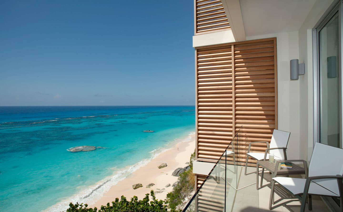 A balcony with two chairs overlooking a beach.