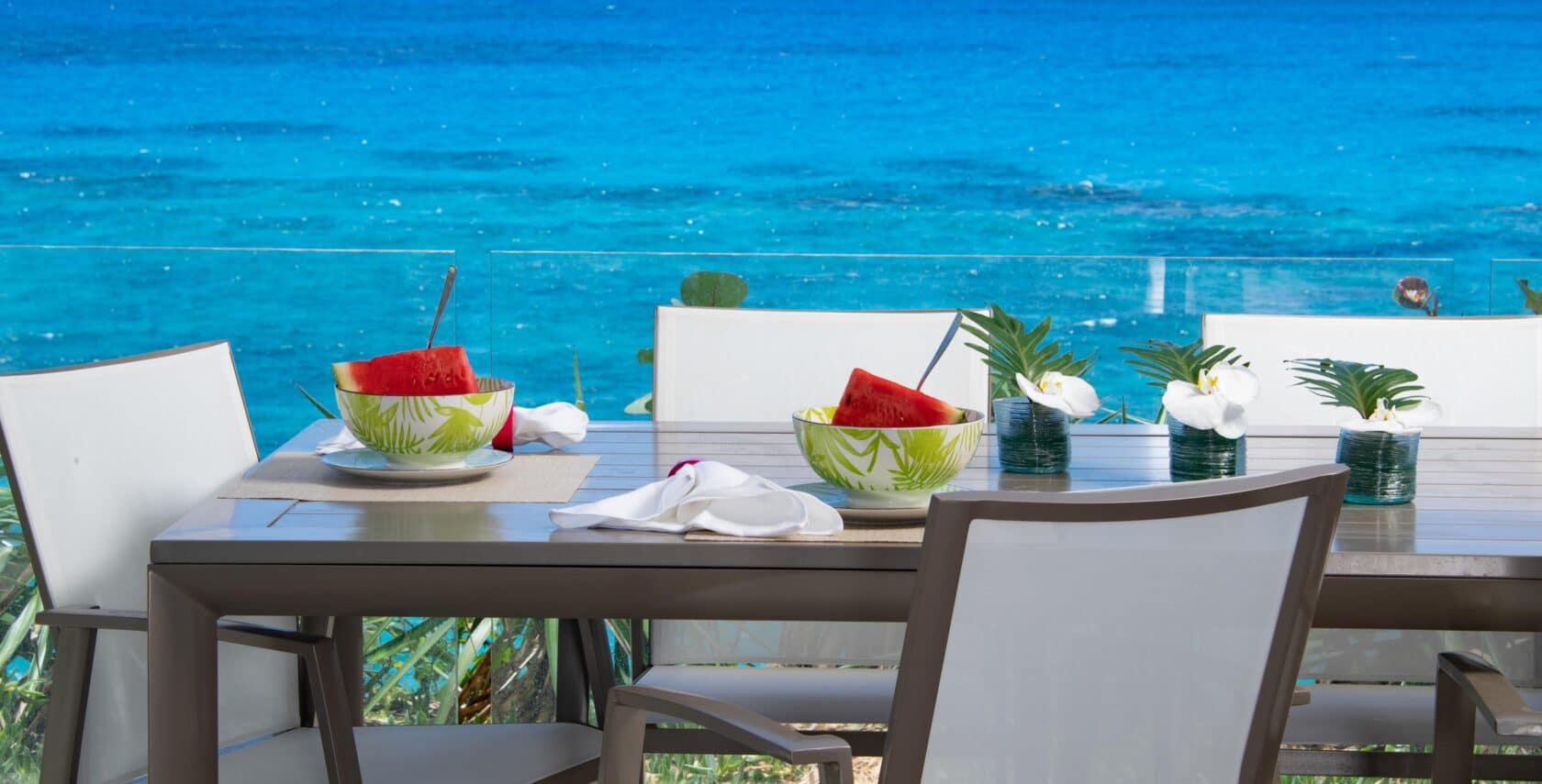 A dining table outside with a view of the ocean in the background.