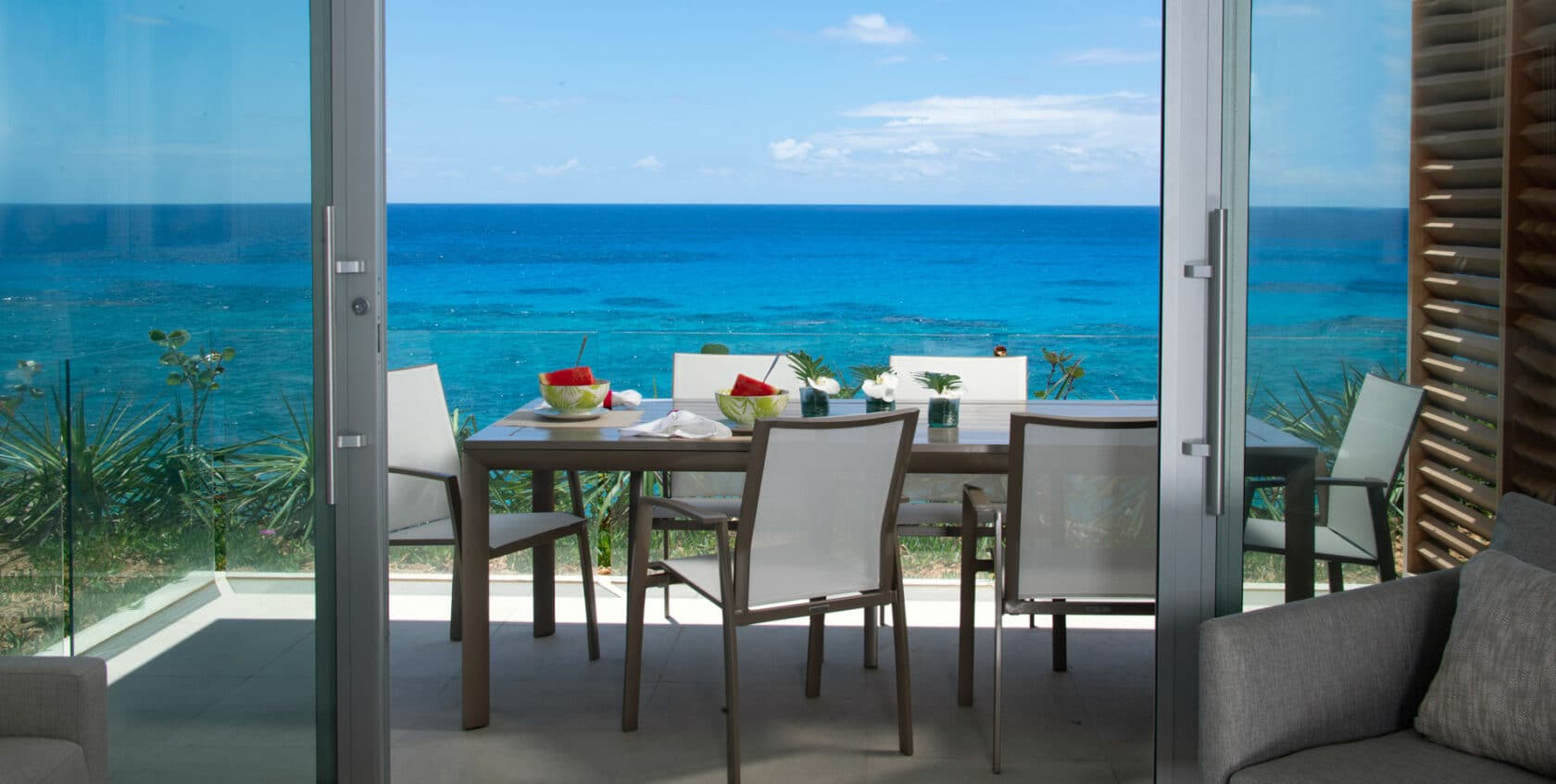A patio with a dining table set with watermelon, with an ocean view in the background.