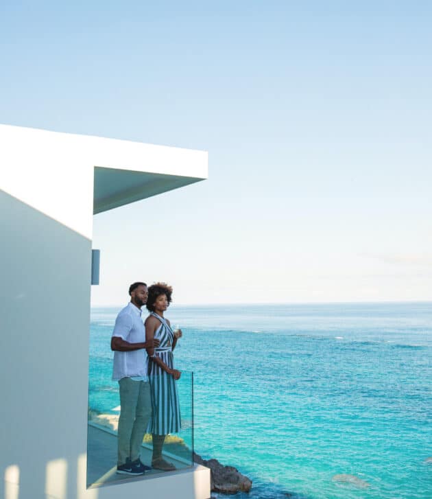 A couple standing together on a balcony overlooking the ocean.