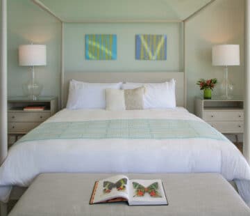 A canopy bed with lamps on either side, along with an open book on a bed bench.