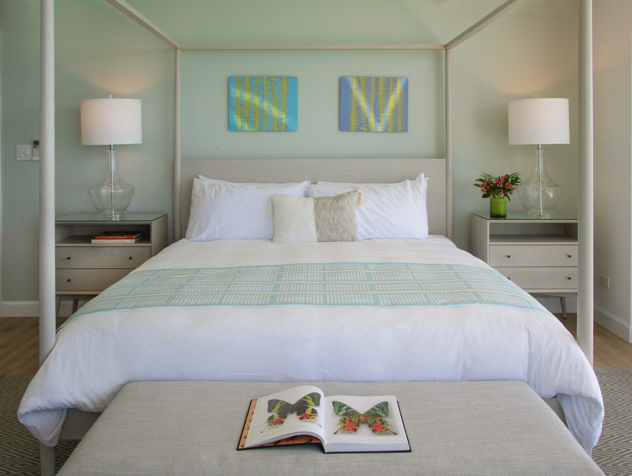 A canopy bed with lamps on either side, along with an open book on a bed bench.