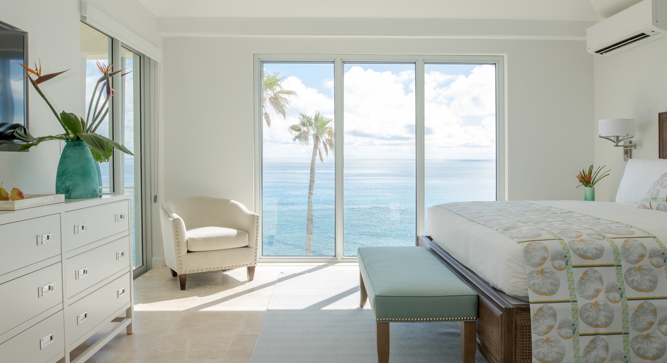 A white bedroom with sliding glass doors with a view of the ocean.