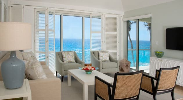 A living room with various chairs, and glass doors with a view of the ocean.