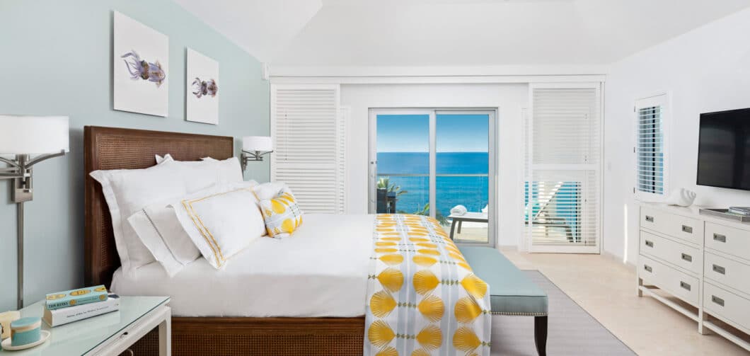 A bedroom with sliding glass doors showing a view of the ocean.