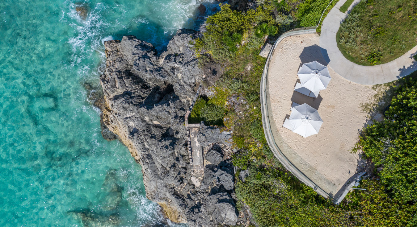 An aerial view of the ocean, rocks, and two parasols.