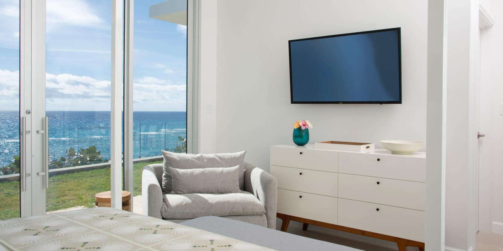 A bedroom with a dresser, chair, TV, and sliding glass doors.