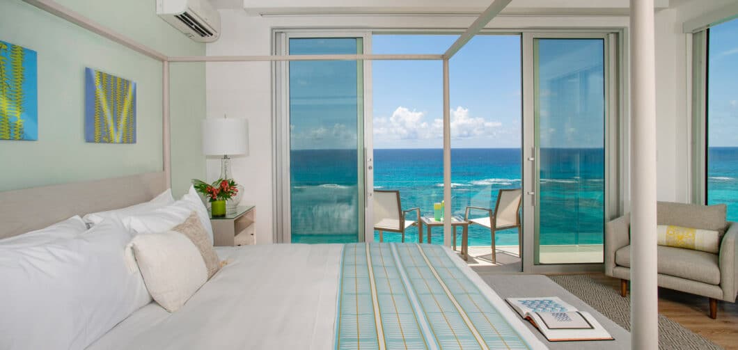 A bedroom with a canopy bed and sliding glass doors leading to a deck overlooking the ocean.