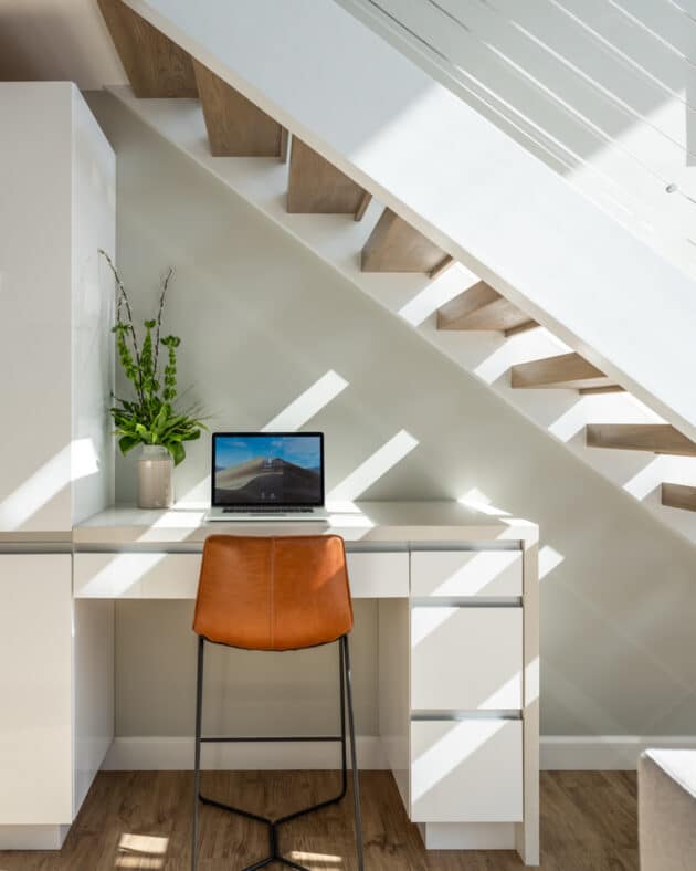 A desk with an open laptop below a staircase.
