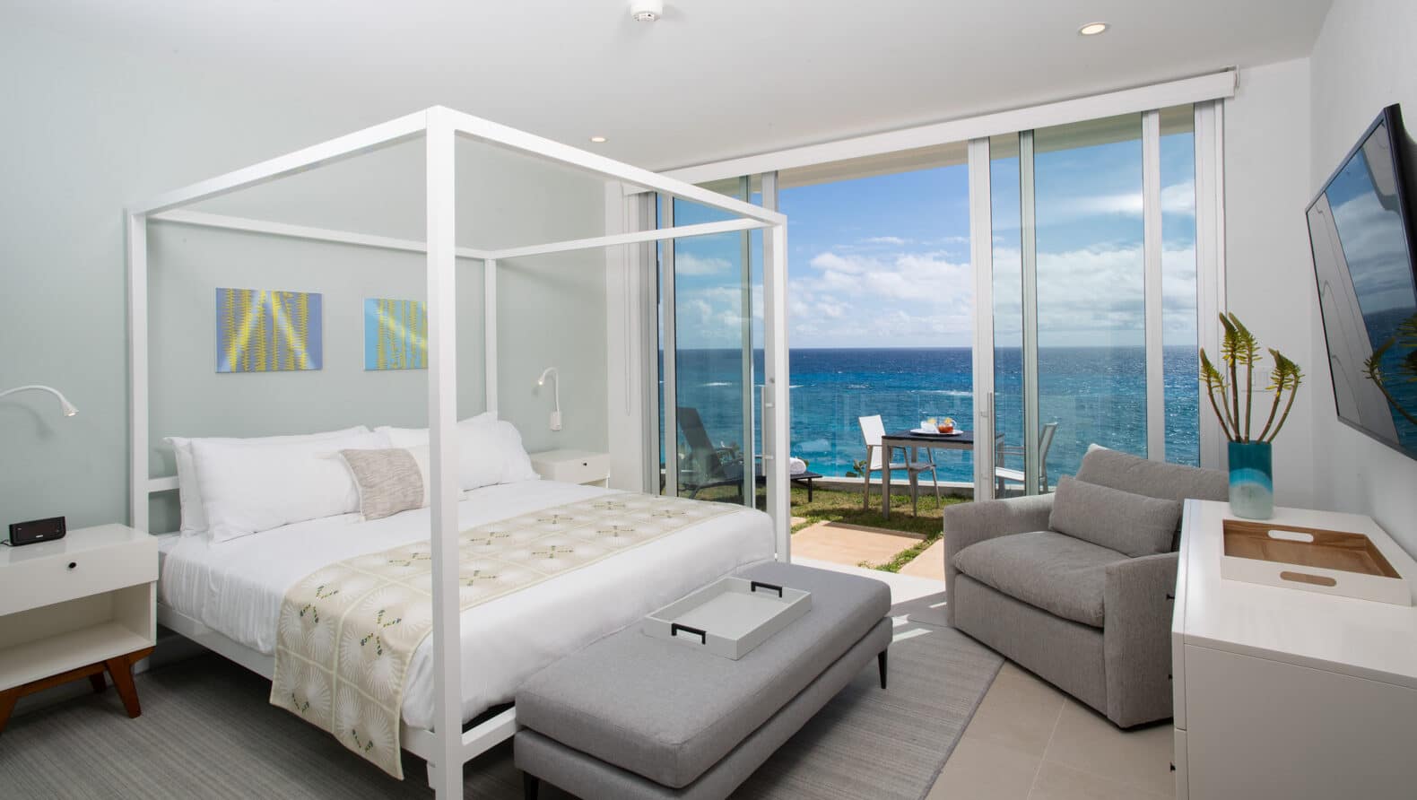 A bedroom with a canopy bed and large glass doors with an ocean view.
