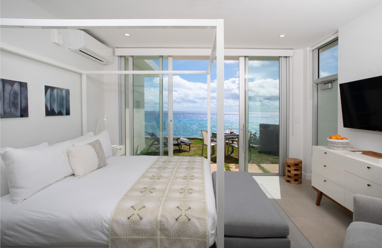 A bedroom with sliding glass doors leading to a patio overlooking the ocean.