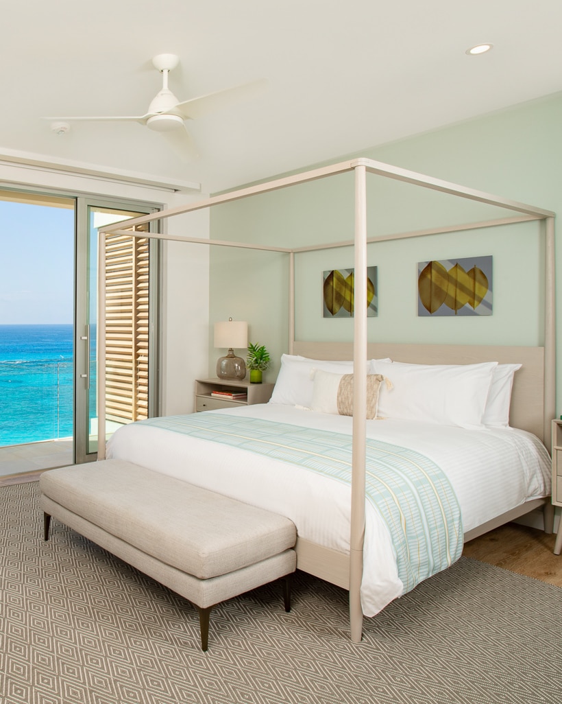 A bedroom with a canopy bed and glass doors with an ocean view.
