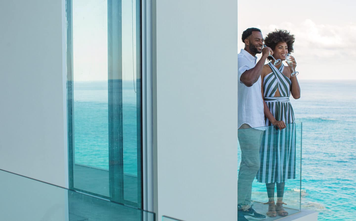 A couple drinking champagne on a balcony overlooking the ocean.