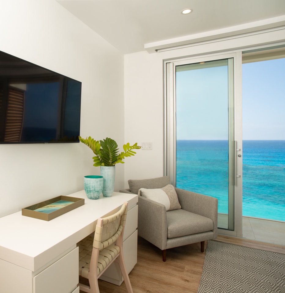 A desk with a TV on the wall in front of it, along with sliding glass doors displaying an ocean view.