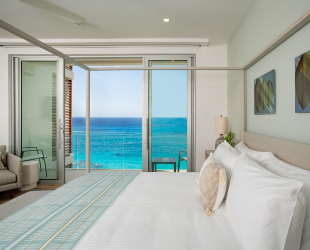 A bedroom with large glass doors with an oceanfront view.