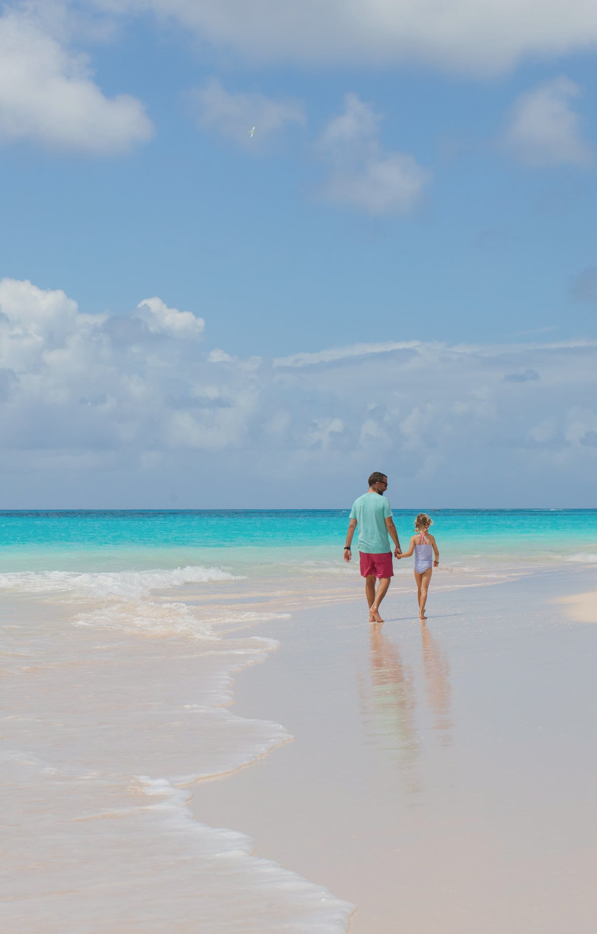 A child holding hands and walking on a beach with her father.