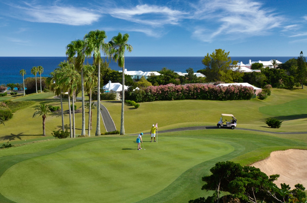 A golf course with palm trees and the ocean in the background.