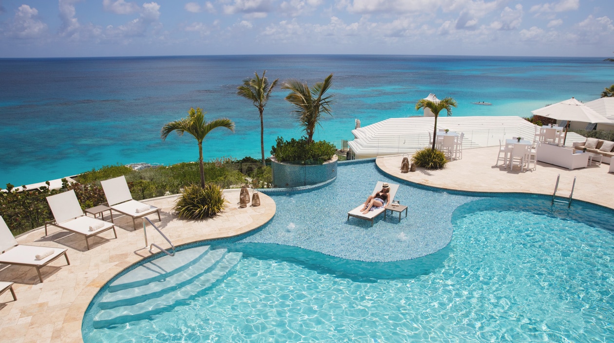 A person relaxing next to a pool overlooking the ocean.