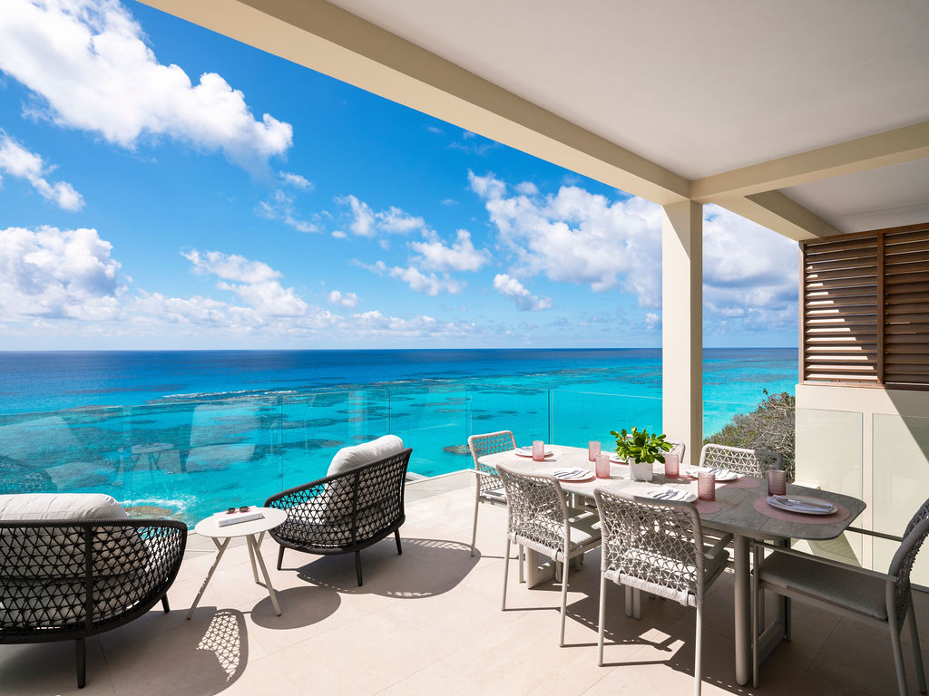 Outdoor balcony with a table and chairs, overlooking a bright blue ocean and clear sky with scattered clouds in a luxury hotel Bermuda.