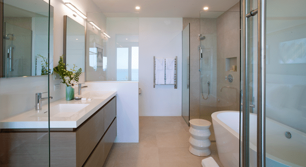 Modern bathroom reminiscent of a luxury hotel in Bermuda, featuring a double sink vanity, glass-enclosed shower, freestanding bathtub, and neutral-toned walls and floors. A towel rack and elegant decor items add finishing touches.