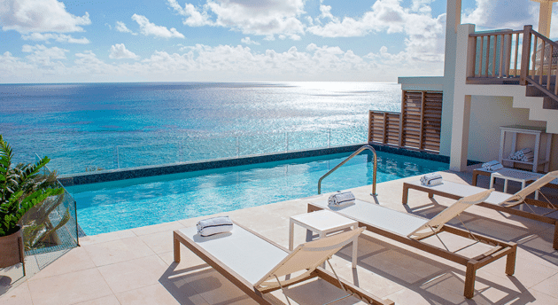 A seaside poolside deck with lounge chairs and towels overlooks a calm blue ocean under a partly cloudy sky, embodying the charm of Bermuda boutique hotels.